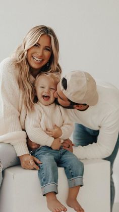 a man, woman and child are sitting on a white bench smiling at the camera