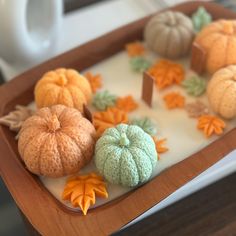 a tray filled with different types of pumpkins on top of a table next to a white coffee cup