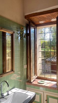 a sink and window in a room with green tiles on the walls, and wood trim around the windows