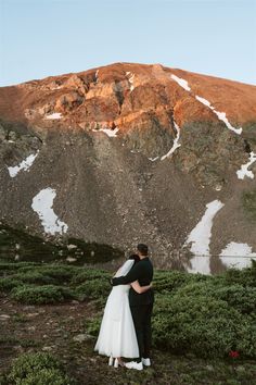 a bride and groom standing in front of a mountain with snow on the mountainside