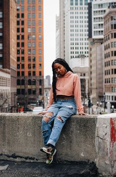 a woman sitting on top of a cement wall next to tall buildings in the city