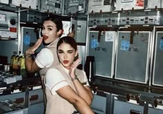 two women are posing in front of some electrical equipment and one is touching her face