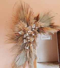 an arrangement of dried flowers and leaves in a vase on a table next to a wall