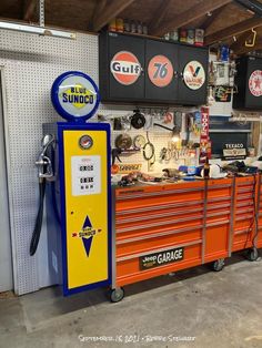 an orange and blue toolbox sitting next to a gas pump in a garage with signs on the wall