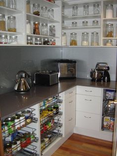 a kitchen with white cabinets and shelves filled with bottles, cans and other items on the counter