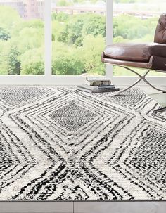 a living room with a chair, rug and large window looking out onto the city