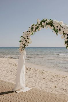 a wedding arch with white flowers on the beach