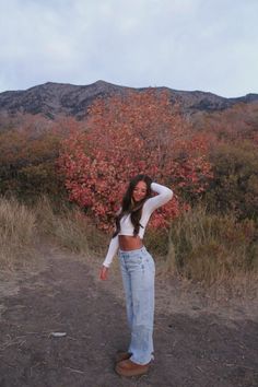 a woman standing in the dirt with her arms behind her head and hands on her hips