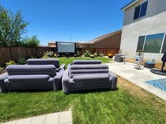 two couches sitting on the grass in front of a backyard with a movie screen