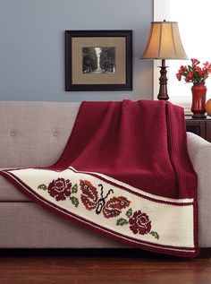 a couch with a red and white blanket on top of it next to a lamp