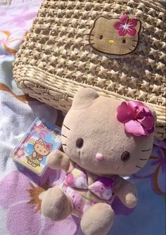 a hello kitty stuffed animal sitting next to a wicker purse on a beach towel