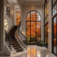 an elegant foyer with large windows and stairs leading up to the second floor that overlooks autumn trees