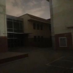 an empty parking lot in front of a large building with windows on each side and dark clouds overhead