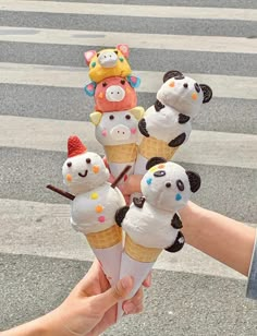 a hand holding an ice cream cone with five stuffed animals on top of it, in the middle of a crosswalk