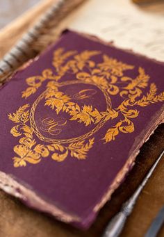 a purple and gold colored book sitting on top of a table next to a fork