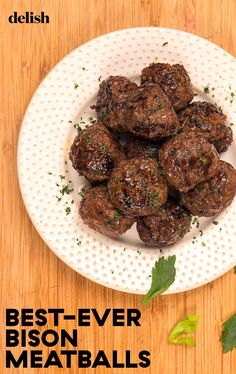 a white plate topped with meatballs on top of a wooden table next to leaves