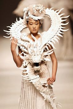 a woman is walking down the runway in a white dress and dragon headdress