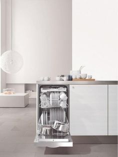 an empty dishwasher in a white kitchen with dishes on the counter and utensils