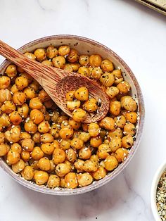 a wooden spoon in a bowl filled with chickpeas and seasoning next to two bowls