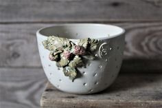 a white cup with flowers on it sitting on top of a wooden table next to a piece of wood