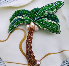 a green brooch with pearls on it and a palm tree pin in the middle