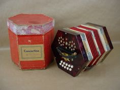 an old red accordion sitting next to a box with the lid open and another item in front of it