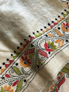 an embroidered piece of cloth with flowers and leaves on the edges, sitting on top of a table