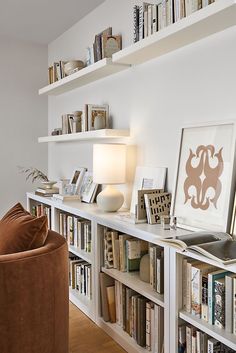 a living room filled with lots of books on top of a white book shelf next to a brown chair