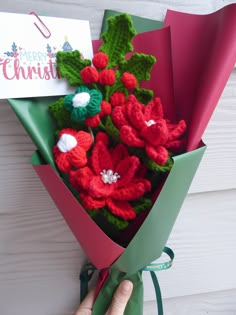 a bouquet of crocheted flowers is wrapped in red and green paper with a hand holding it