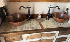 two copper bowls are sitting on top of a wooden cabinet in a bathroom with wood floors