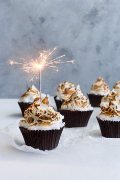 some cupcakes with white frosting and a sparkler sticking out of them