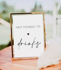 a sign that says help yourself to drinks sitting on top of a wooden table next to a white feather