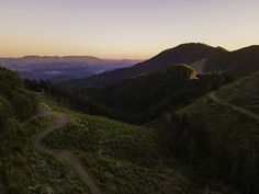 an aerial view of a dirt road in the middle of a mountain range at sunset