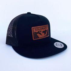 Colorado Elevation mountains faux leather patch in rawhide. Available in silver gray or black. Flat bill cotton twill front. Mesh back with adjustable snapback Urban Trucker Hat With Logo Patch For Outdoor, Black Leather Hats For Outdoor Activities, Urban Adjustable Trucker Hat With Logo Patch, Flat Bill Hat With Logo Patch For Outdoor Activities, Leather Patch Trucker Hat For Camping, Brown Flat Bill Snapback Hat For Camping, Outdoor 5-panel Baseball Cap With Leather Patch, Adjustable Casual Snapback Hat With Leather Patch, Made In Usa Snapback Baseball Cap For Outdoor