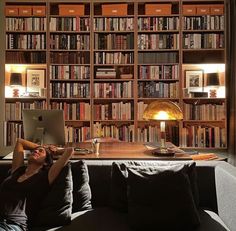 a woman sitting on a couch in front of a bookshelf using a laptop