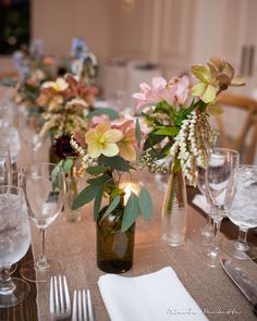 the table is set with wine glasses, silverware and flowers in vases on it