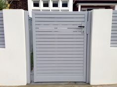 a grey gate with two white pillars in front of a house