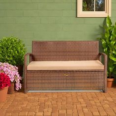 a brown wicker couch sitting on top of a brick floor next to potted plants