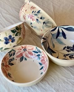 four bowls with floral designs on them sitting on a white tableclothed surface, one is empty and the other two are half full