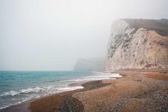 an empty beach next to the ocean with white cliffs in the background and blue water