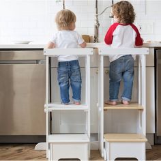 two toddlers are sitting at the kitchen counter and one is on the step stool