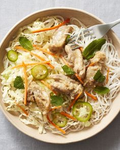 a bowl filled with meat and veggies on top of white noodles next to a fork