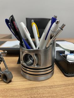 a metal cup filled with pens and pencils on top of a wooden table next to a cell phone