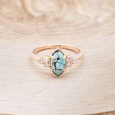 a gold ring with a turquoise stone surrounded by white diamonds on a wooden table top