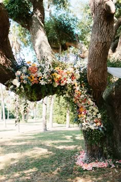 an outdoor ceremony setup with flowers on the tree and white cloth draped over the branches