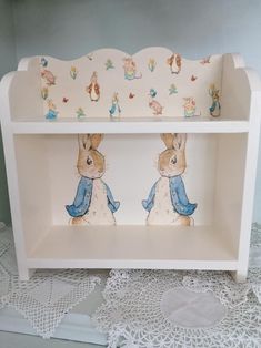 a white shelf with two rabbits painted on the front and back sides, sitting on a lace doily