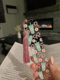 a person is holding up a bookmark with flowers and bows on it in front of a fireplace