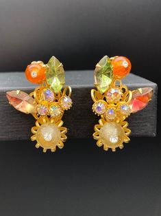 Add a touch of vintage charm to your outfit with these beautiful clip-on earrings. The intricate art glass design features a stunning abstract floral bouquet shape in gold tone metal, with clear, green, pink givre, and orange colors rhinestones. The earrings are perfect for any occasion, and make a great statement piece for any outfit. Length 1 5/8 approx Width 1 inch approx Measuring at 1 5/8 inches in length, these ear climbers are designed to fit comfortably on your ear lobes. The prong setti Vintage Handmade Clip-on Earrings For Party, Vintage Clip-on Earrings For Wedding, Vintage Handmade Clip-on Earrings For Wedding, Handmade Vintage Clip-on Earrings For Party, Handmade Vintage Clip-on Earrings For Wedding, Antique Clip-on Earrings For Party, Vintage Handmade Clip-on Earrings For Evening, Vintage Clip-on Earrings For Vintage Events, Mid-century Clip-on Earrings For Party