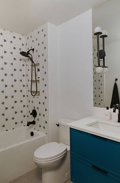 a white toilet sitting next to a bath tub under a bathroom mirror on top of a blue cabinet