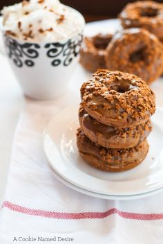 three chocolate donuts stacked on top of each other next to a cup of whipped cream